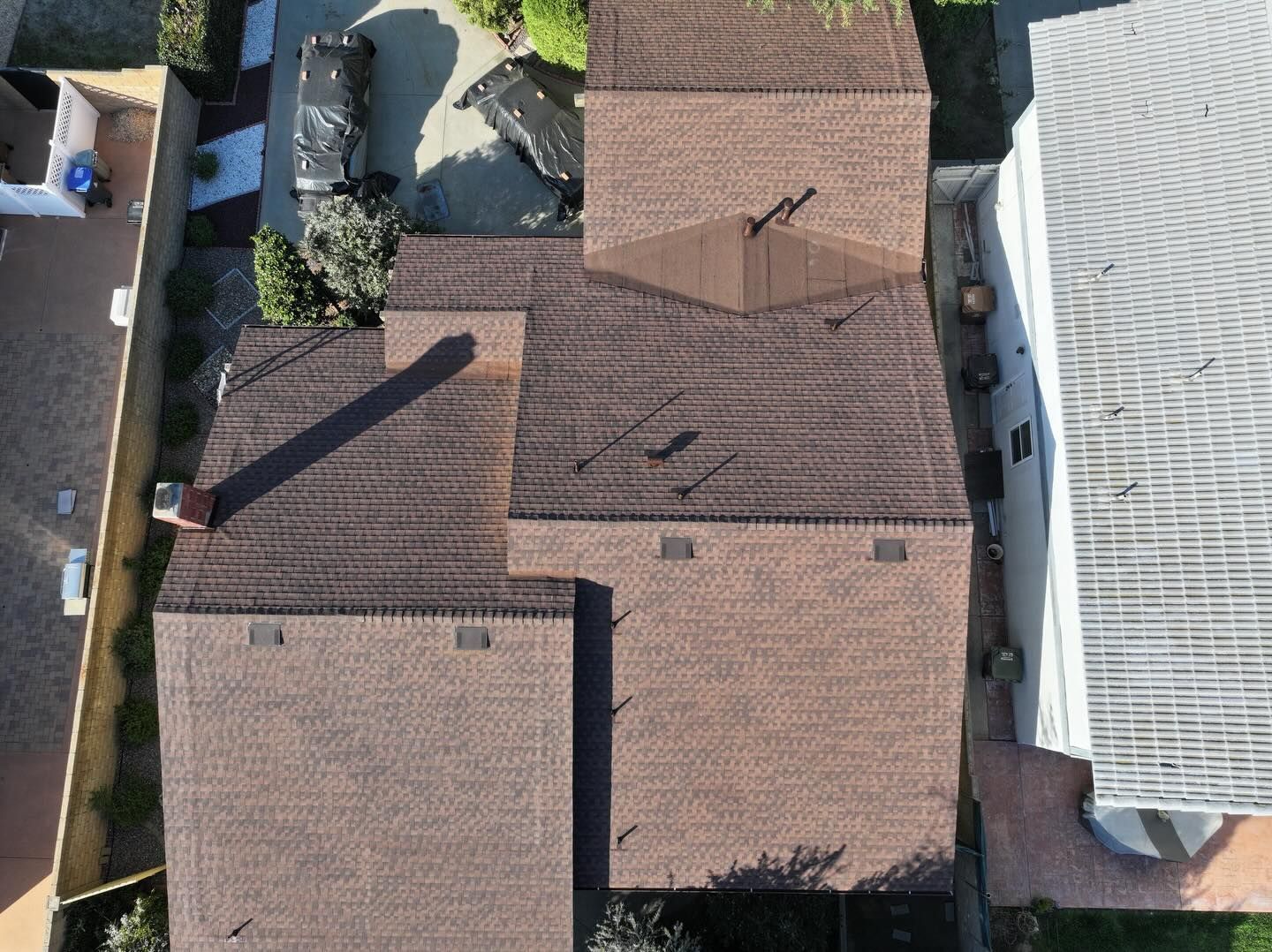 An aerial view of a dark shingled residential roof with multiple slopes, a chimney, and several vents.