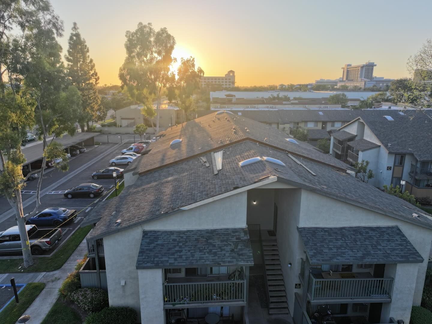 An elevated view of apartment buildings and a parking lot at sunset, with golden light reflecting off rooftops.