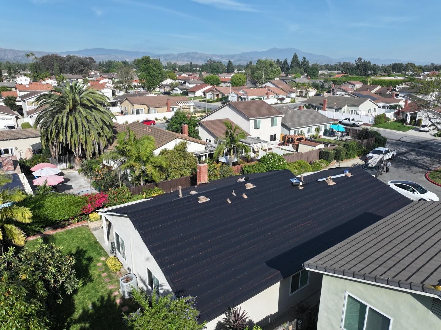 An aerial view of a suburban neighborhood featuring a house with a newly installed black roof under a clear blue sky.