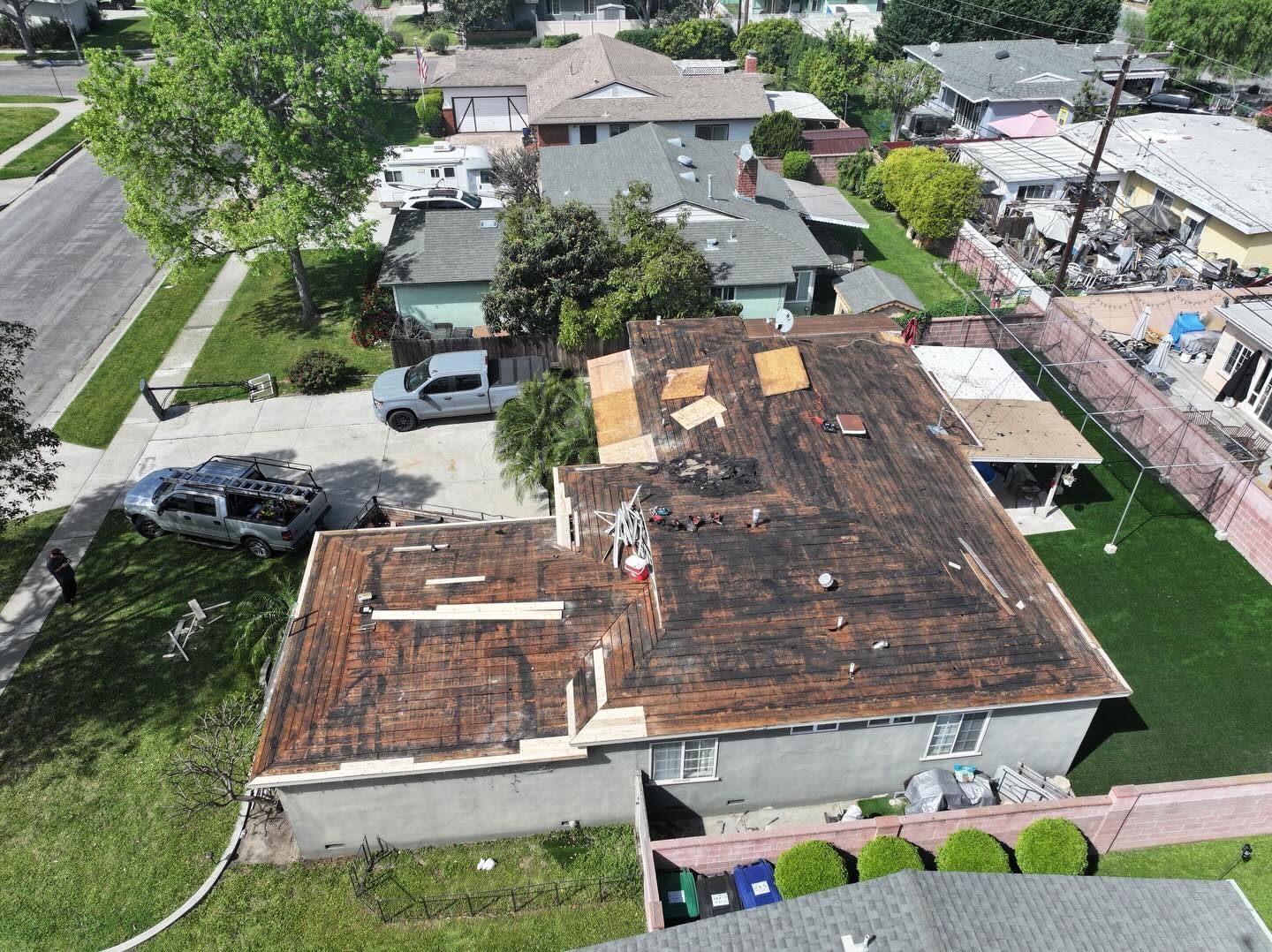 An aerial view of a house undergoing roof replacement, showing bare roof decking, construction materials, and a driveway.
