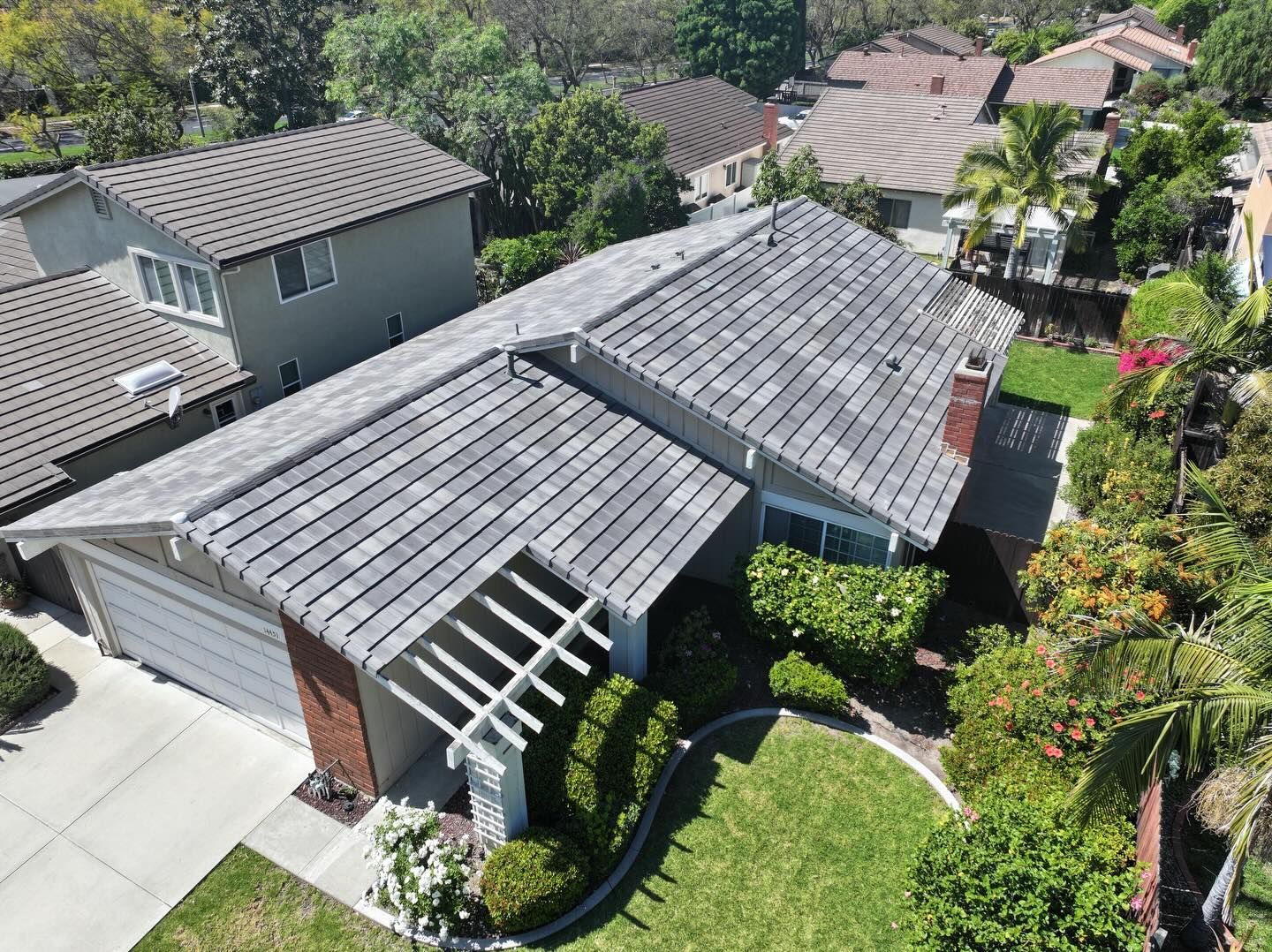 High-angle view of a gray-roofed single-story residential home with a pergola, driveway, and front lawn.