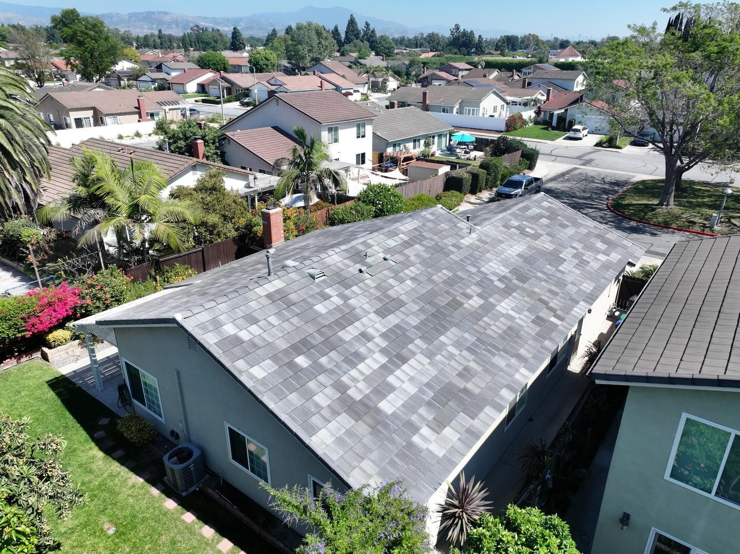 Aerial view of a residential neighborhood with gray roof tiles, lush green trees, and houses in a suburban setting.