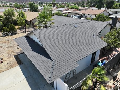 An aerial view of a grey shingled roof on a suburban house with a concrete driveway and surrounding residential area.