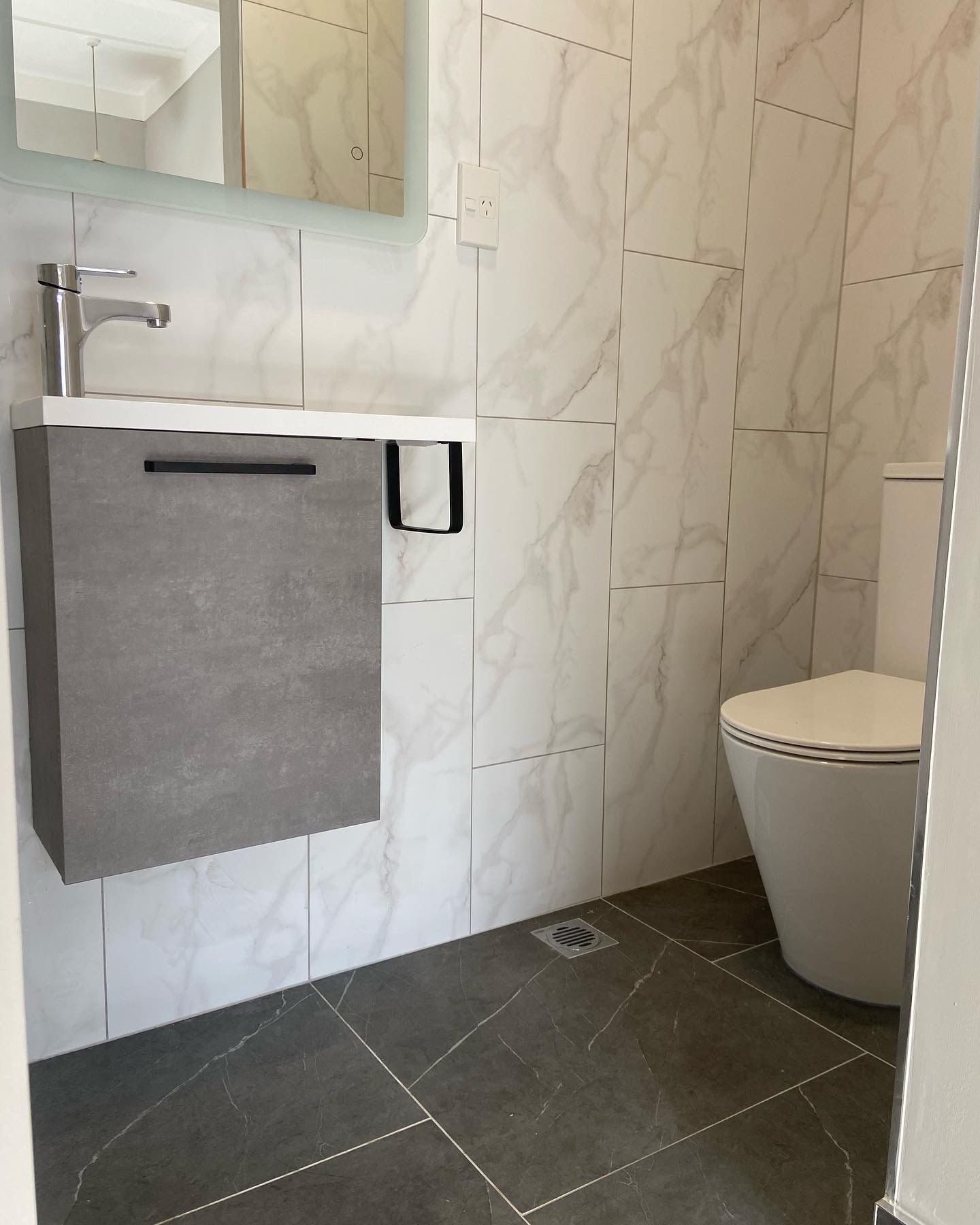 Modern bathroom with gray vanity, toilet, and marble-patterned tiles.