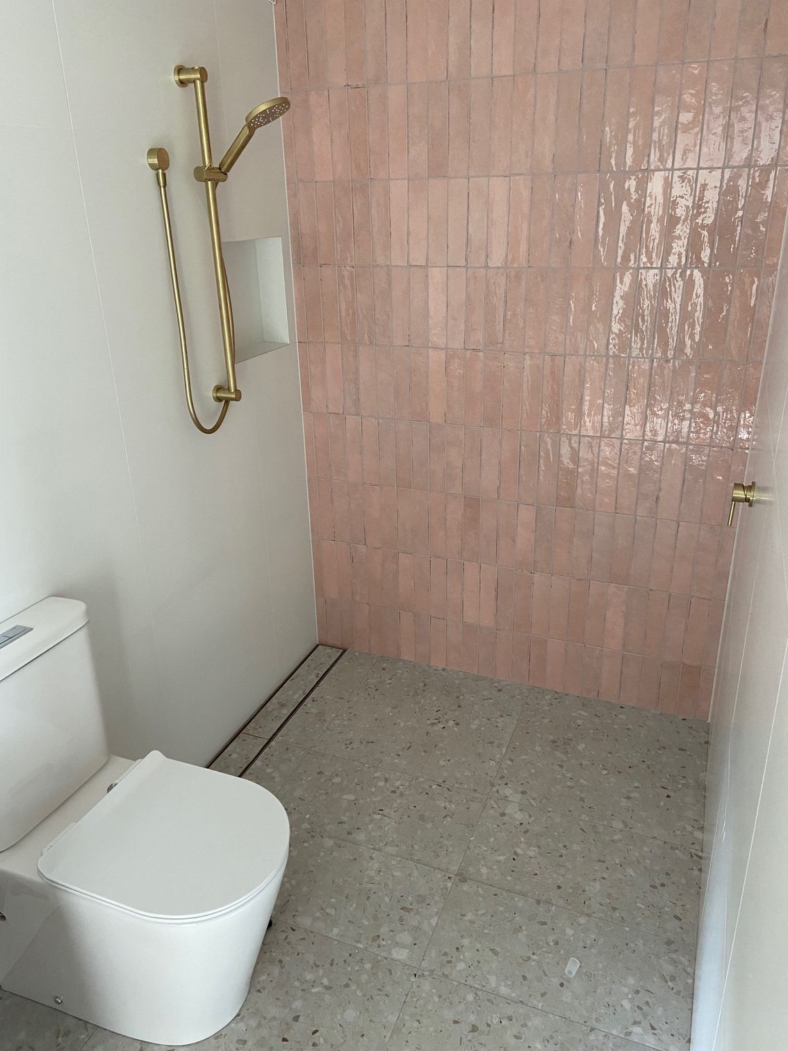 Small bathroom with pink tiled shower wall, gold shower fixtures, and a white toilet.