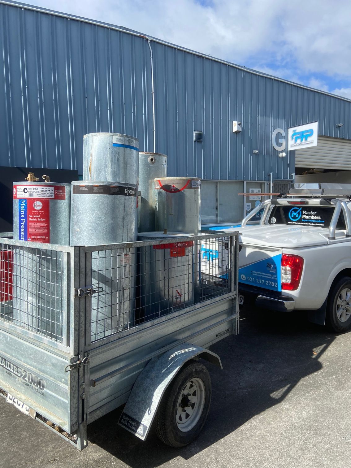 Trailer loaded with metal barrels and a white pickup truck in front of a building.