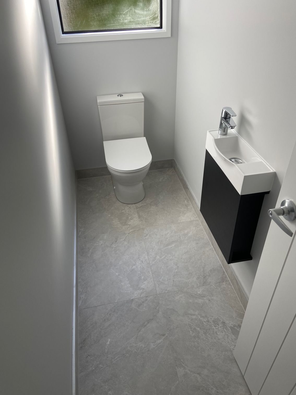 Small, modern powder room. Toilet centered, dark vanity with small sink, gray floor, white walls.