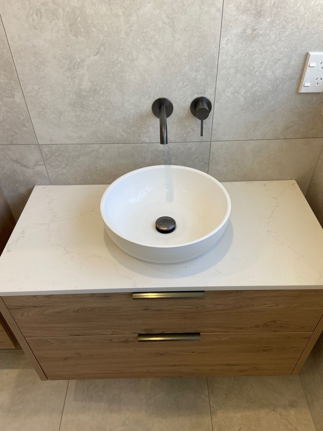 Bathroom vanity with a white vessel sink on a wooden cabinet, with gray faucet fixtures and light-colored countertops.