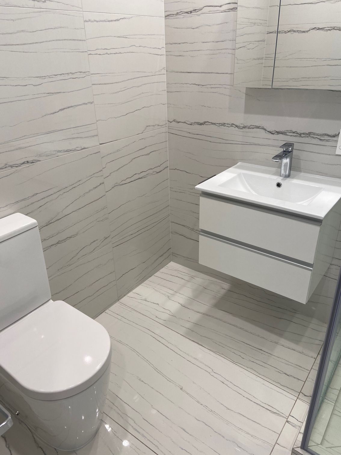 Modern white bathroom with toilet, floating sink, and tiled walls/floor.