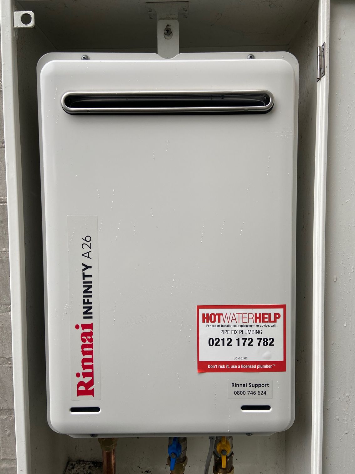Rinnai Infinity A26 hot water heater in a white box, mounted on a brick wall.