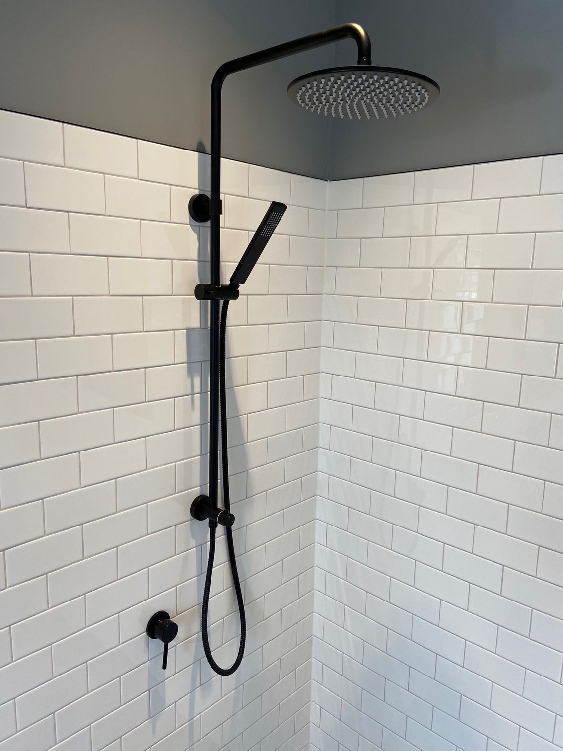 Black shower fixture on white tiled wall in a bathroom.
