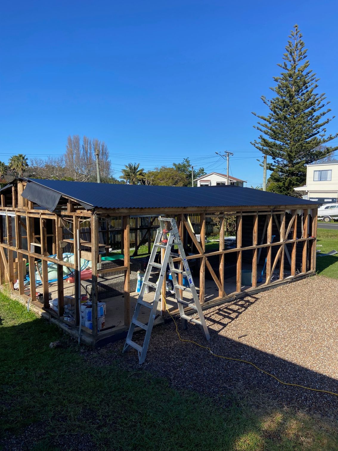 Wooden structure under construction with a partially completed dark roof; a ladder stands in front.