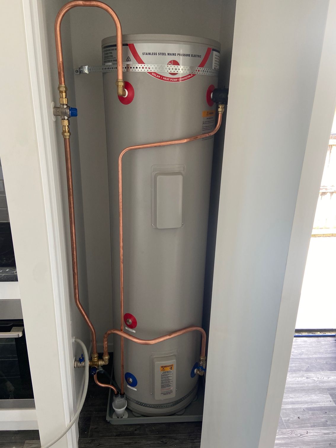 A hot water heater in a white cabinet with copper pipes connected to it.