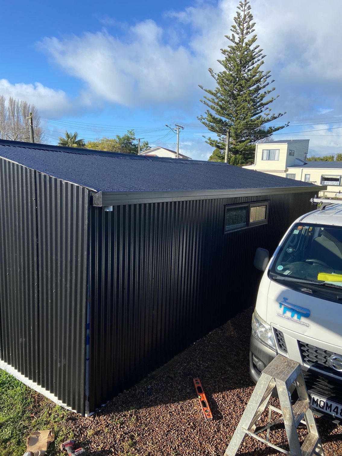 Black corrugated metal shed with a dark roof, next to a van.