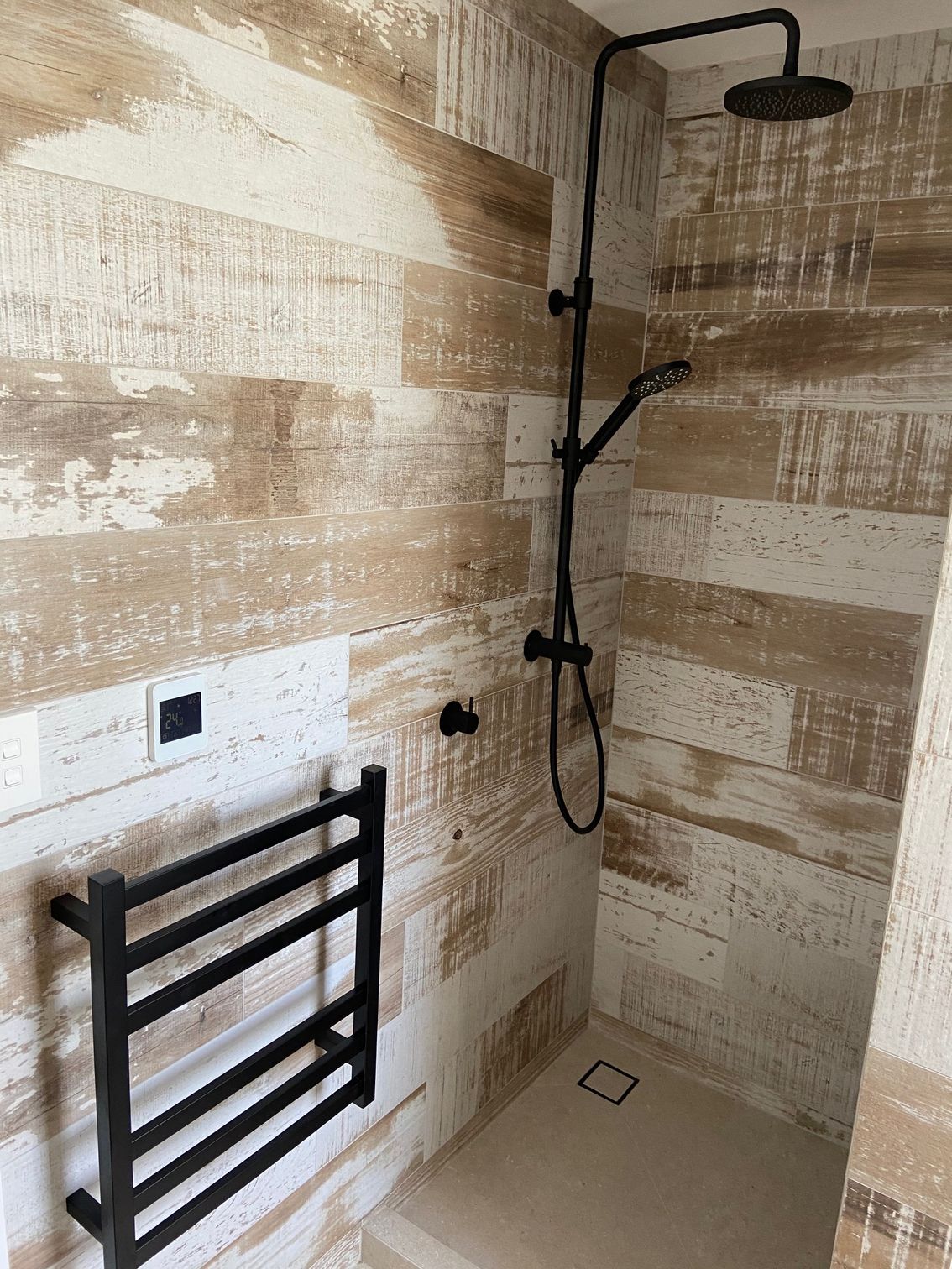 Shower with black fixtures and wood-look tile walls. Heated towel rack and controls on the left.