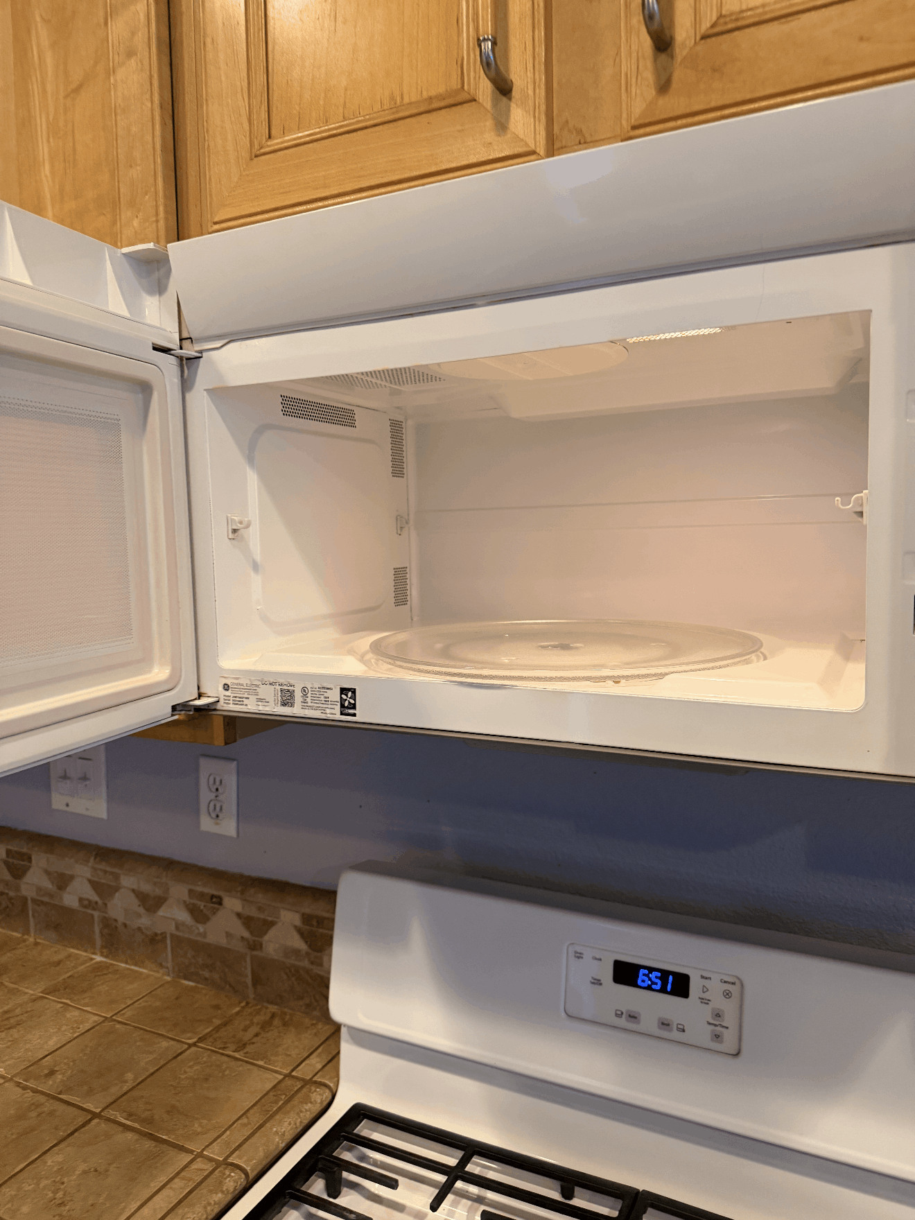 Empty open white refrigerator with freezer compartment, kitchen cabinets above and control panel below.