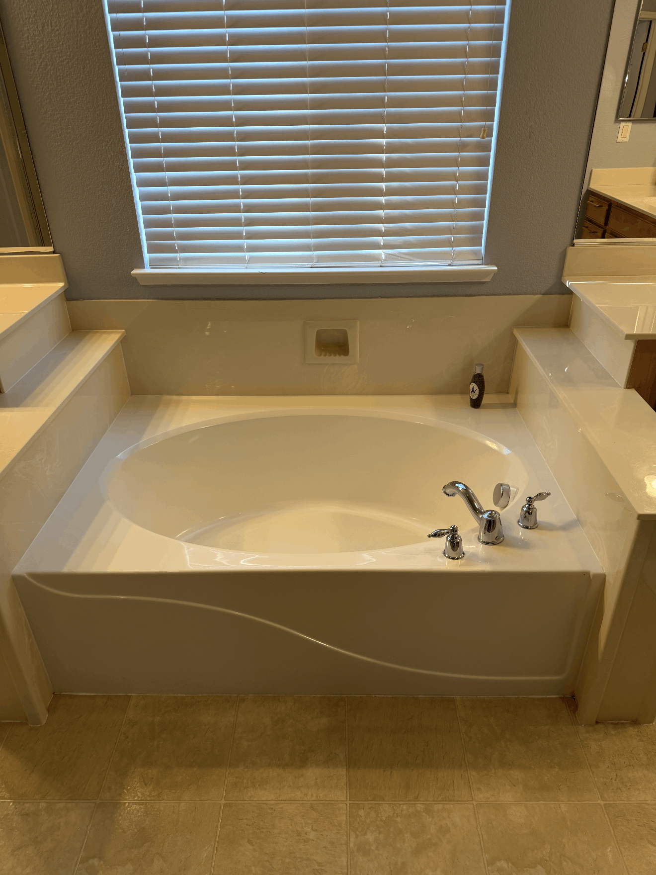 Built-in bathtub with chrome fixtures beneath a window and blinds