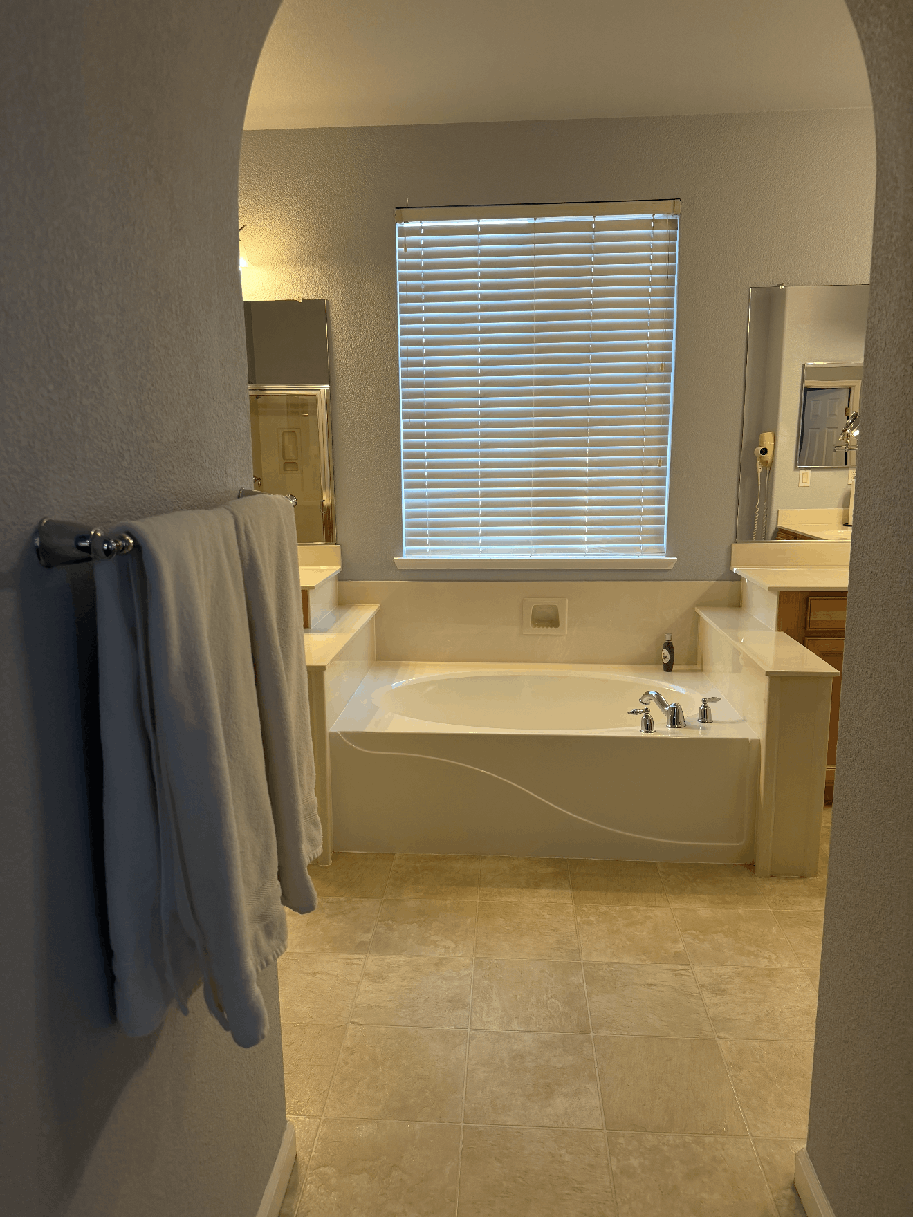 Bathroom with a freestanding tub beneath a window, viewed through an arched doorway, with towels hanging on the left.