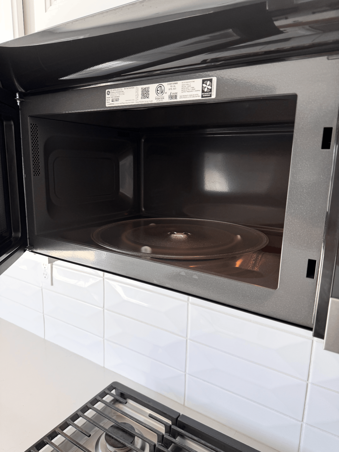 Open microwave oven above a white tiled backsplash, with a stovetop below.