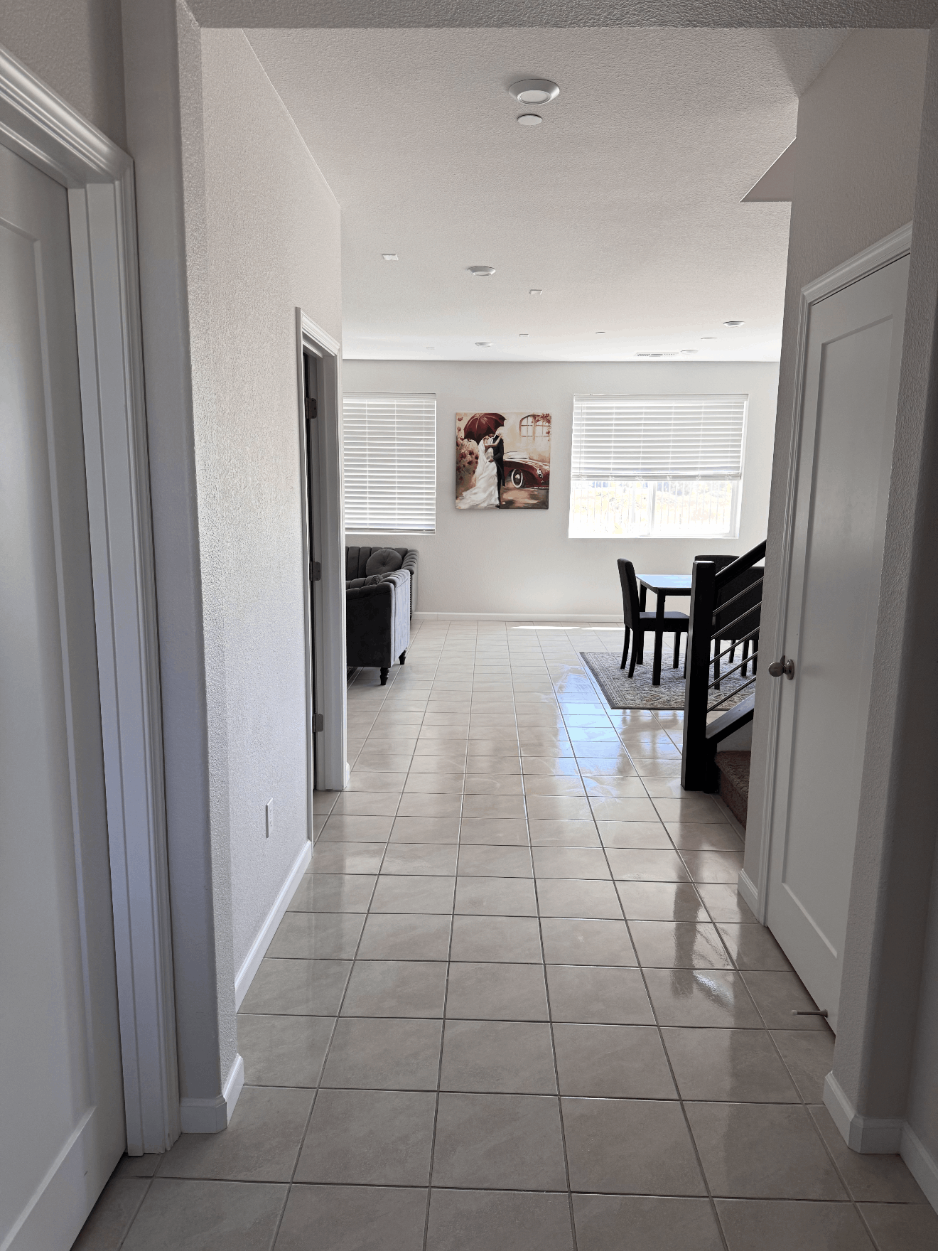 Hallway with tiled floor leading to a bright dining area with a table, chairs, and windows.