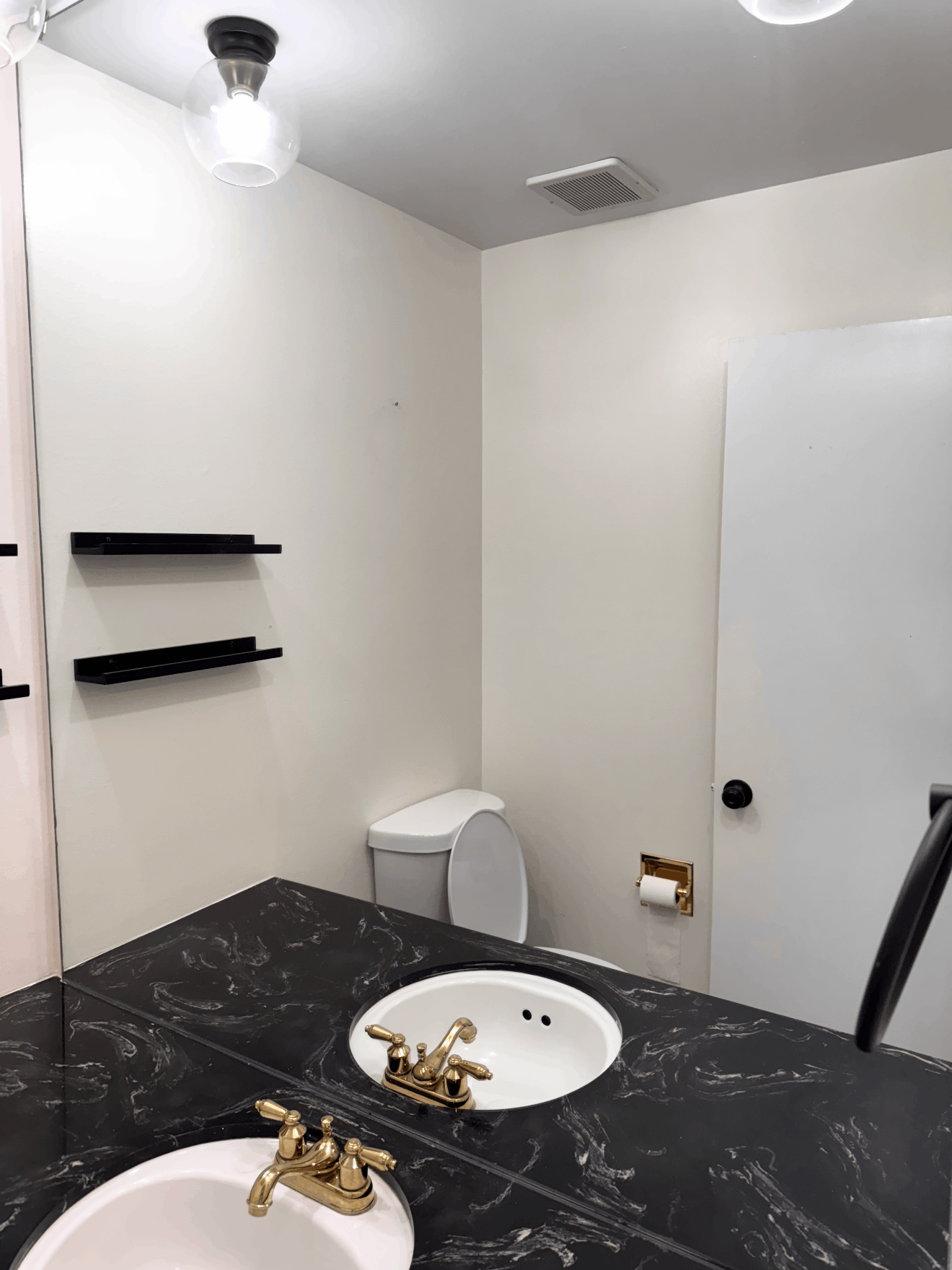 Small bathroom with white walls, black marble vanity, round sink, toilet, and wall shelves.