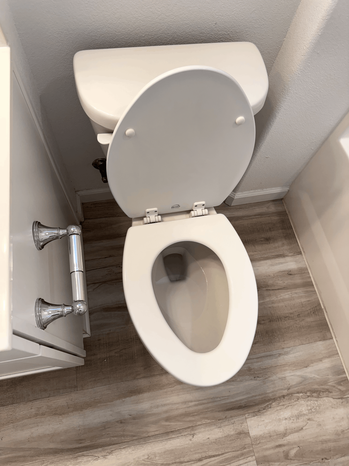Open toilet in a small gray restroom with a sink cabinet beside it.
