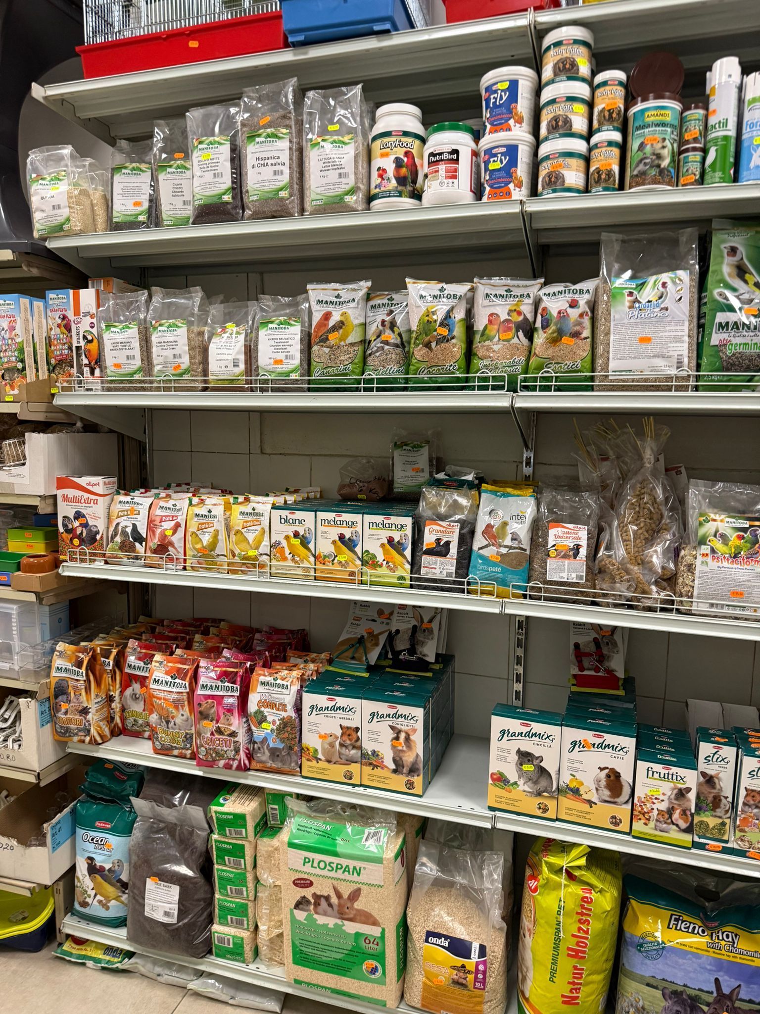Scaffali di un negozio di articoli per animali domestici pieni di sacchi e contenitori di mangime per uccelli, snack e accessori per piccoli animali.