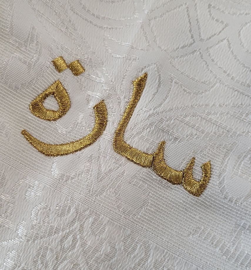 Gold embroidered Arabic script on white fabric, reading