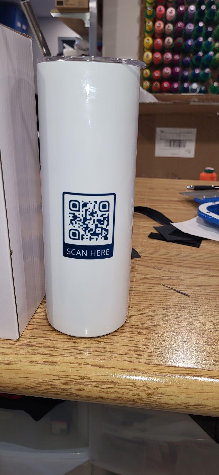 White tumbler with a QR code sticker on a wooden desk.