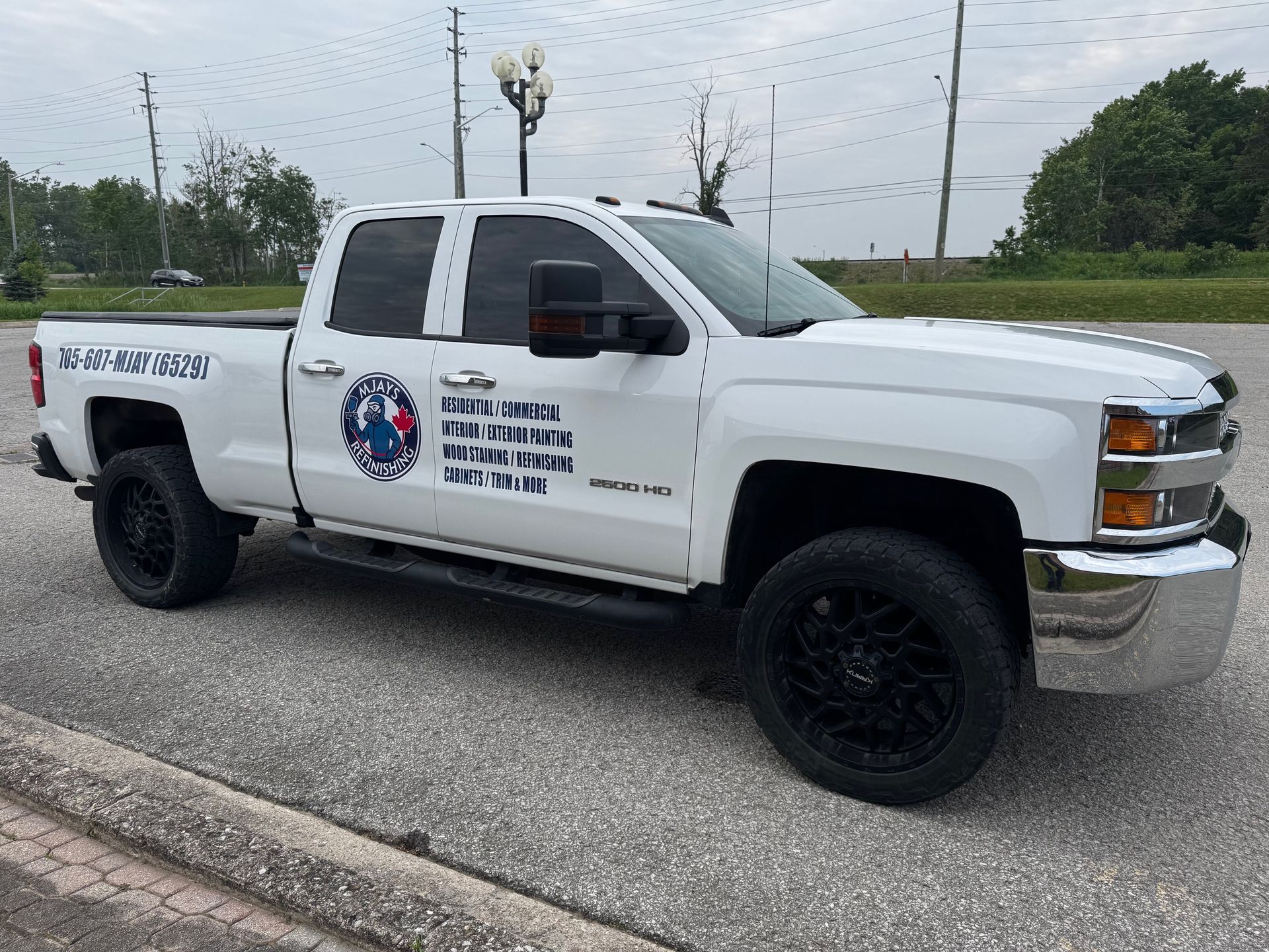 White pickup truck with black wheels, parked on asphalt, with business logo on the door.