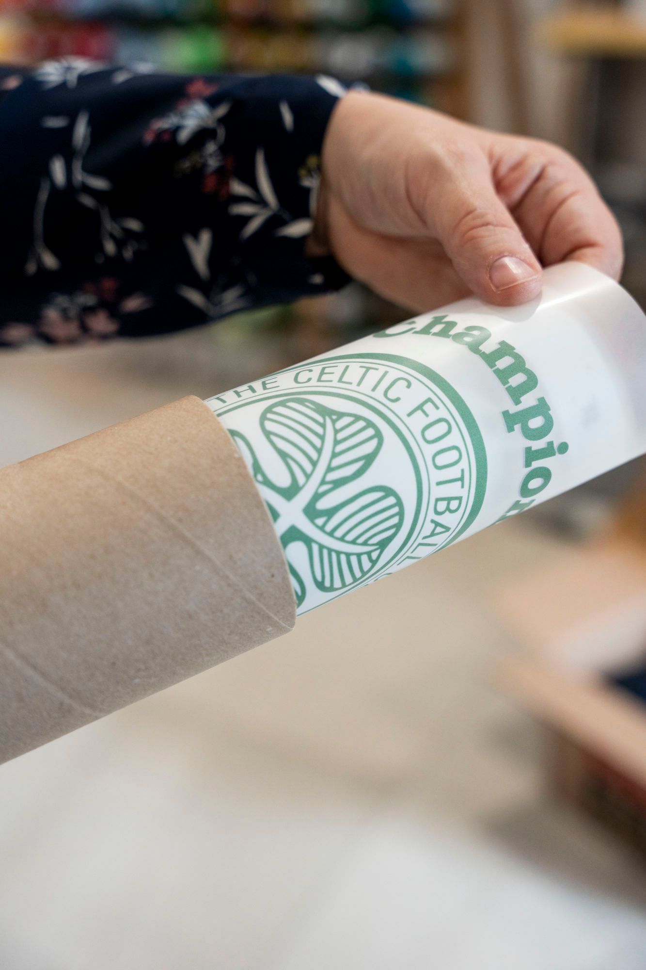 roll of dtf transfers getting shipped. A hand holds a rolled poster of the Celtic Football Club logo.