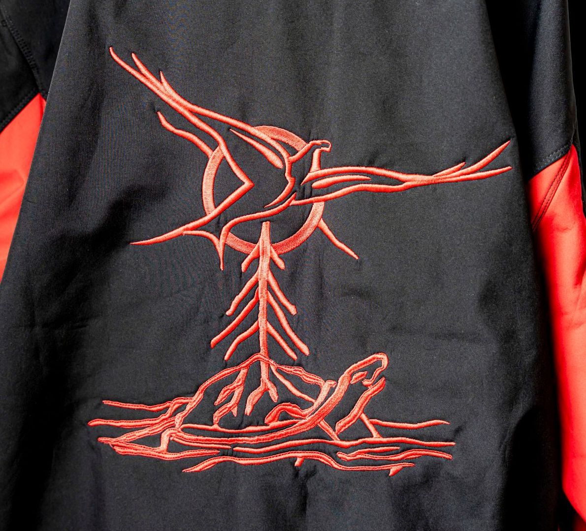 Red embroidered bird above a stylized tree and a turtle on a black jacket.