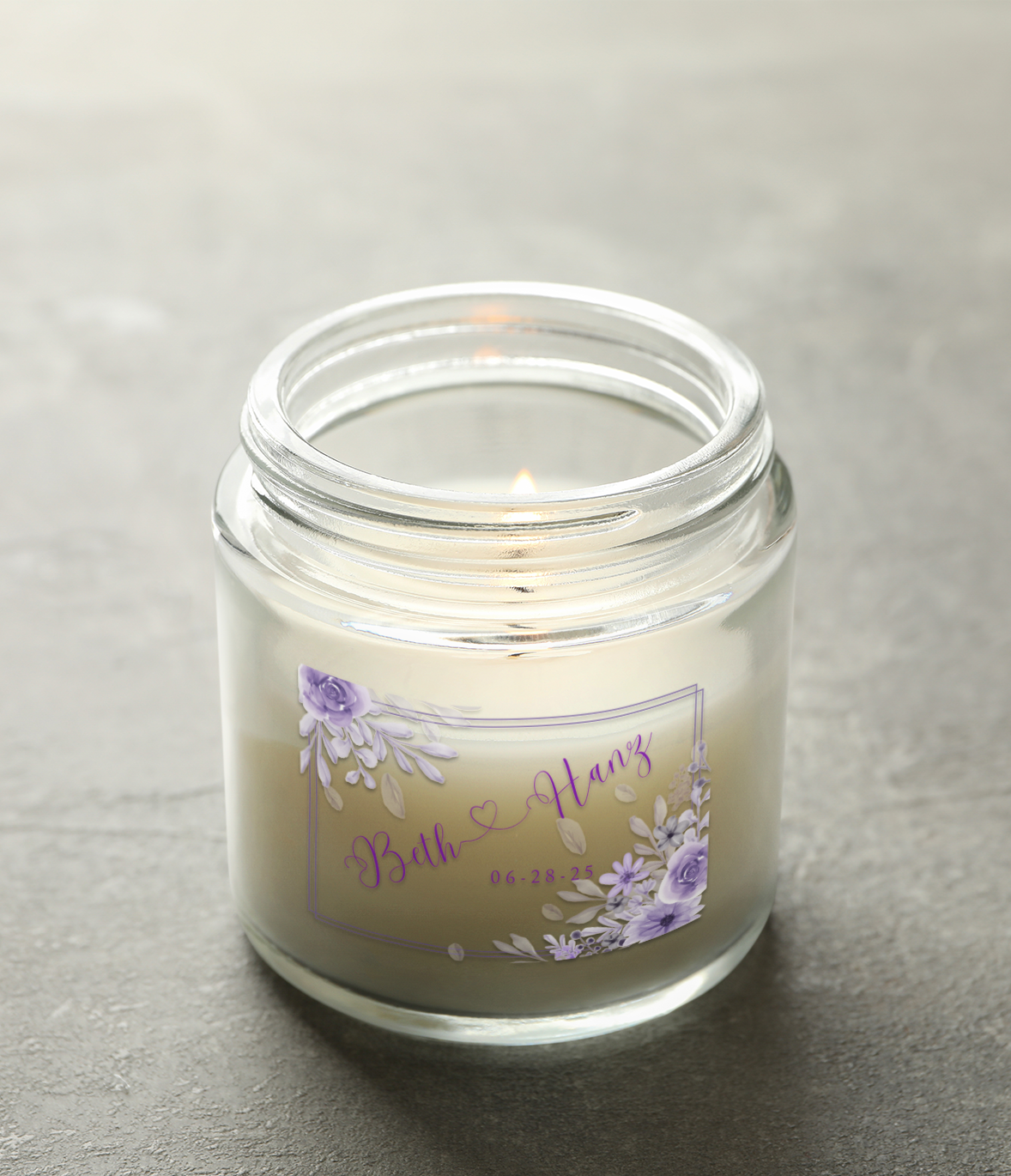 Glass candle with purple floral label. Text on label says “Beth & Henry” and a date.