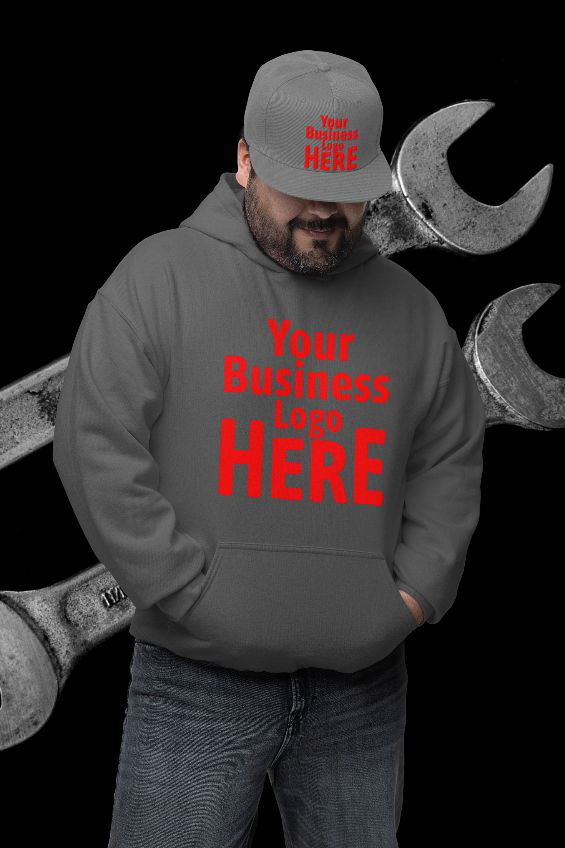 Man in gray hoodie and hat with text, hands in pockets, with wrenches in background.