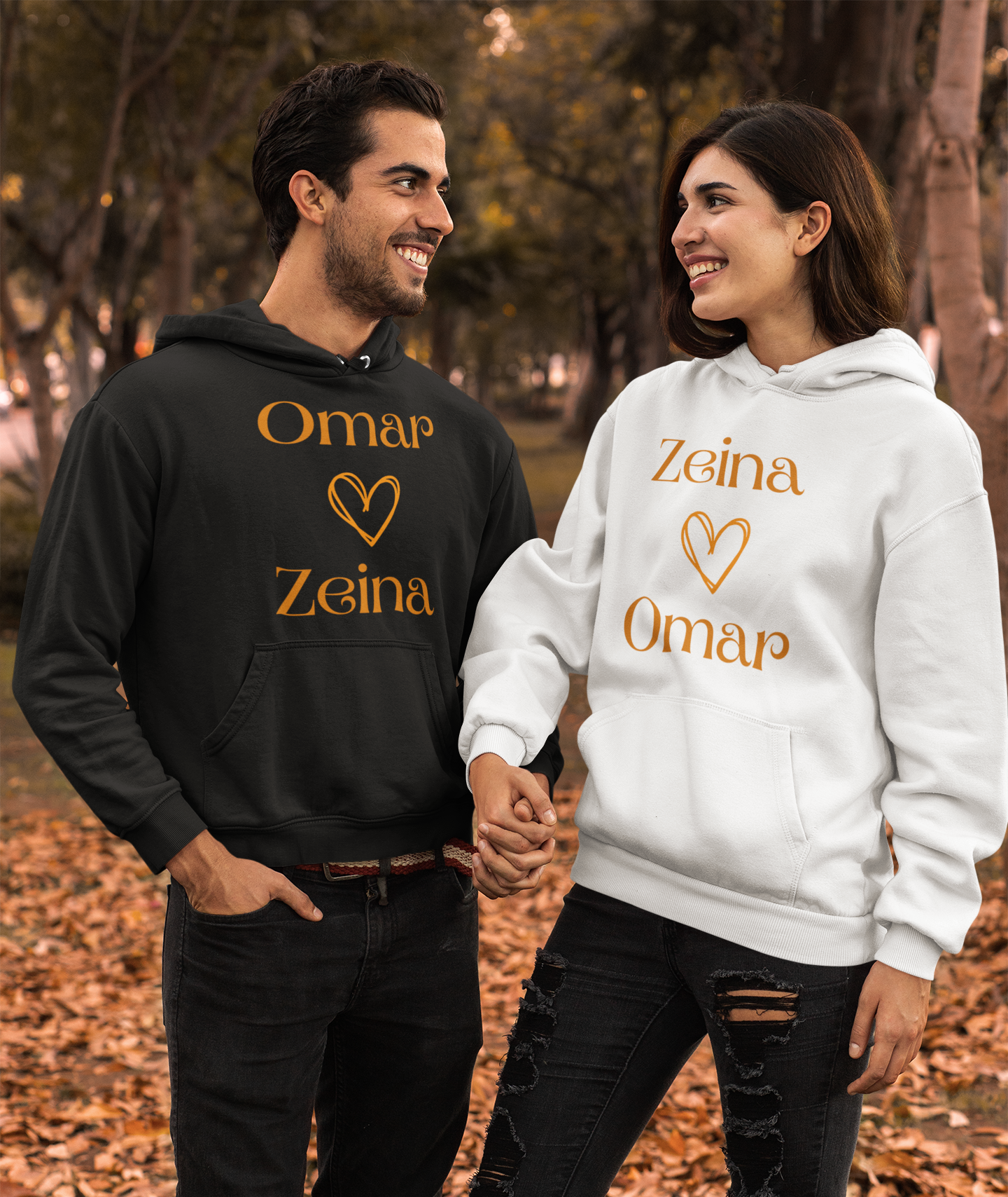 Couple wearing matching hoodies, holding hands. Hoodie: Omar over Zeina with heart. Hoodie: Zeina over Omar with heart.