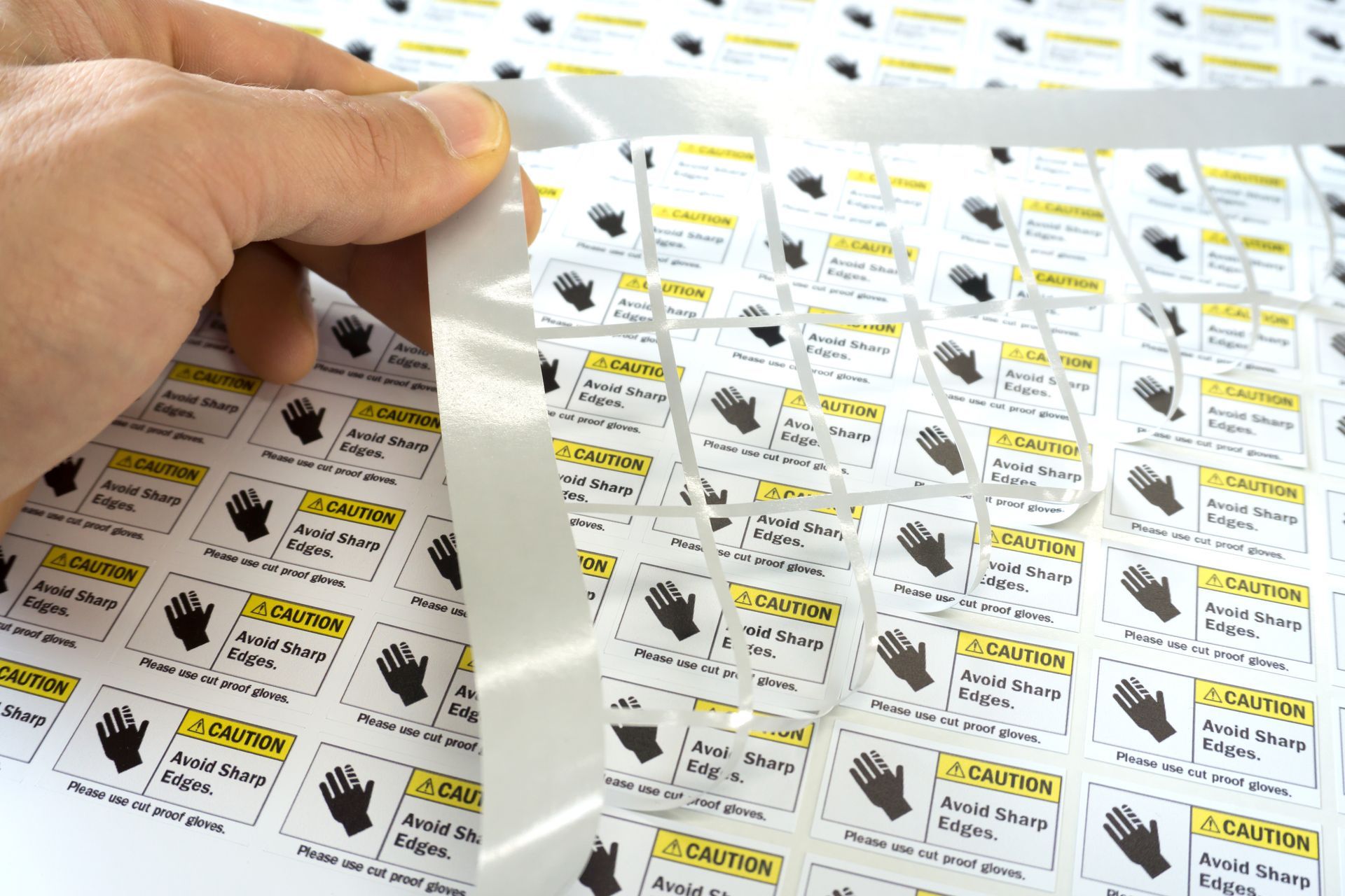 Hand peeling a sheet of pre-cut adhesive labels with yellow and black text and a hand symbol.