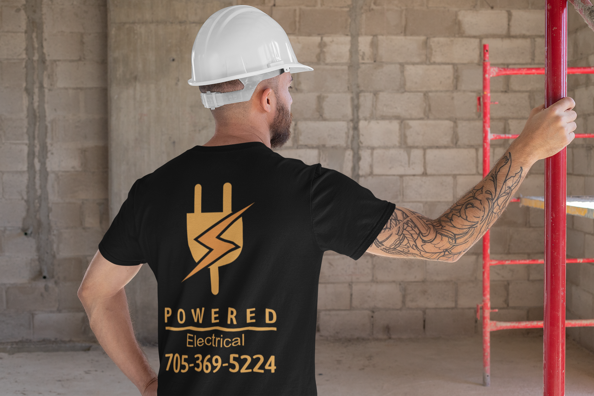 Man in black shirt with electrical logo on construction site, holding a ladder.