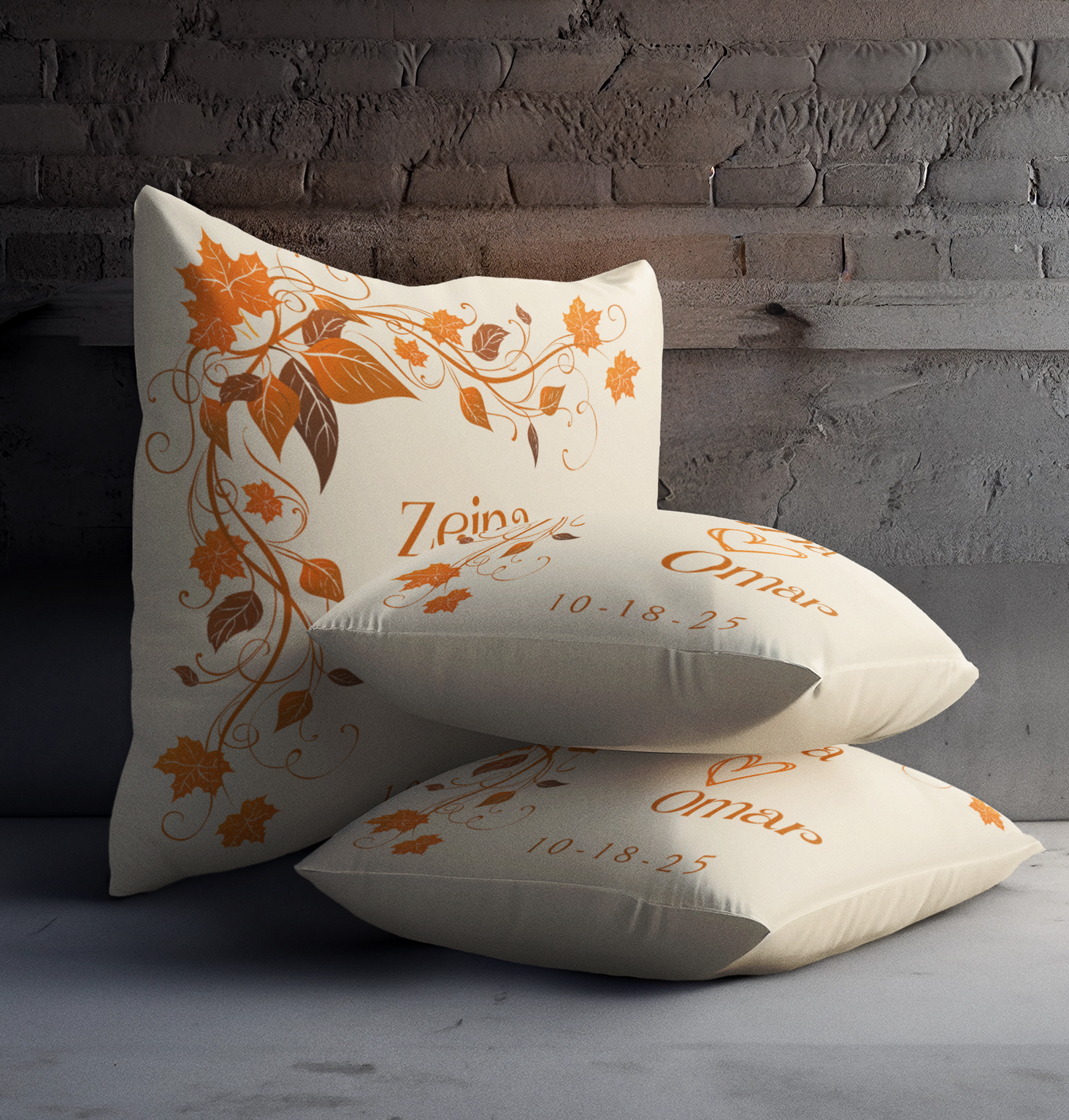 Three off-white pillows with orange floral design and text against a brick wall. Text reads