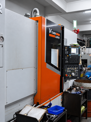 工作坊內的一台橘黑相間的 CNC 機器,旁邊有控制面板和工具