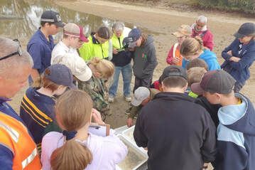Group of people in hats and jackets huddled around a rocky excavation outdoors, inspecting a find