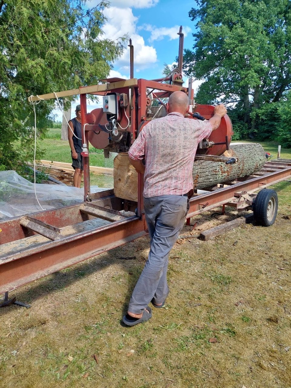 Two men loading a wood-milling machine onto a trailer in a grassy field