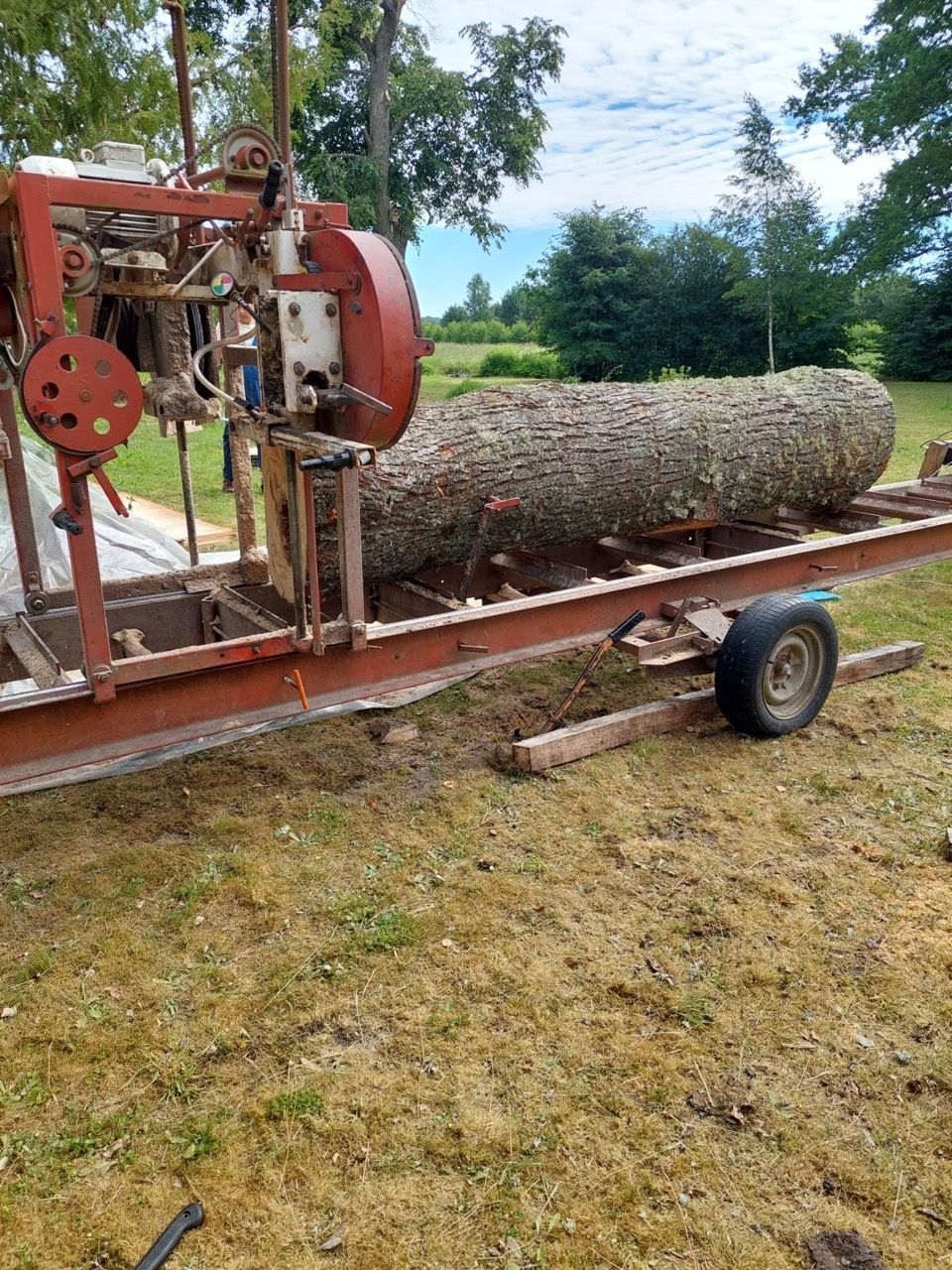 Log splitter loading a large log onto a trailer in a grassy yard