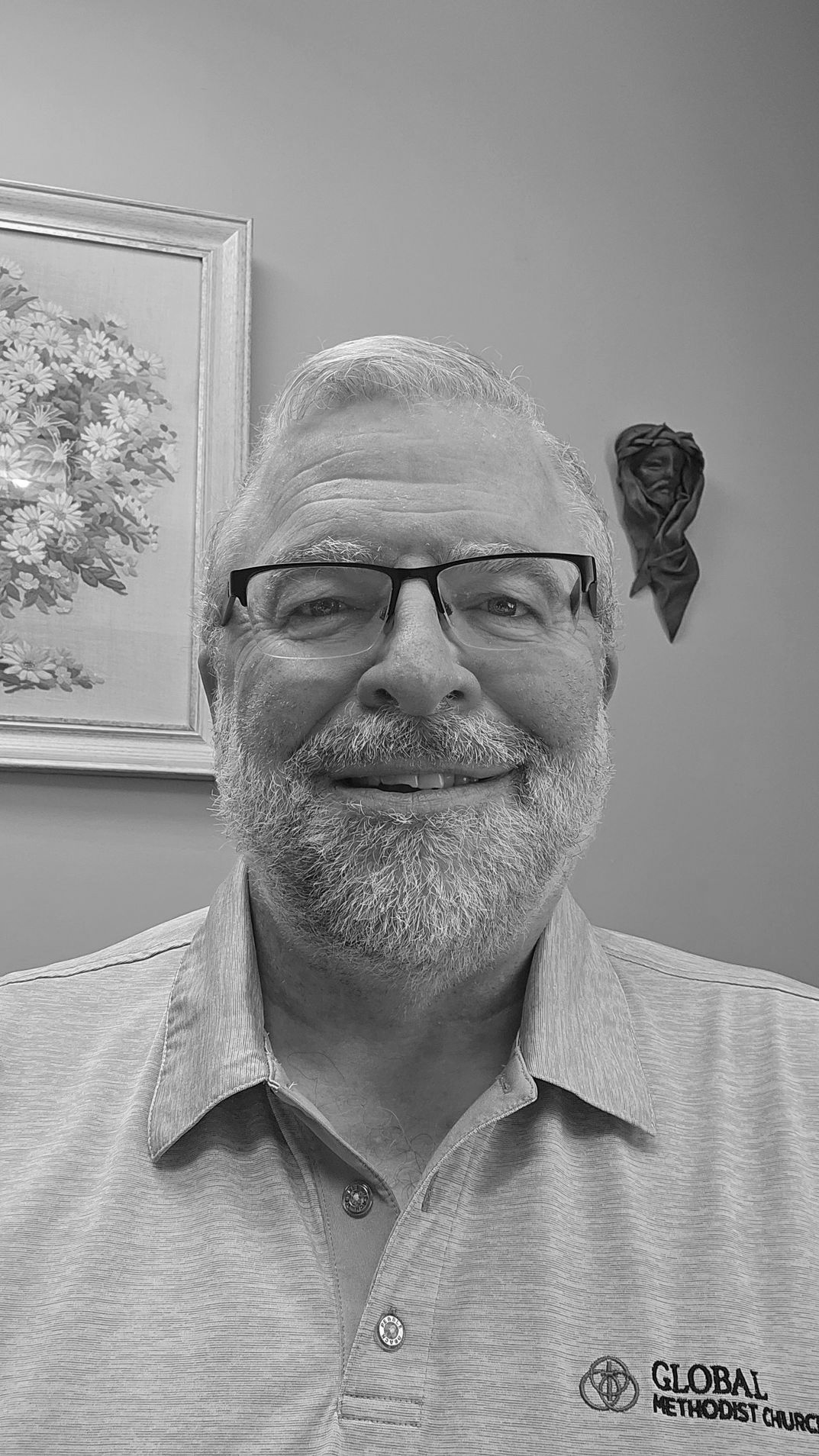 Man with a beard and glasses smiling at the camera, indoors.