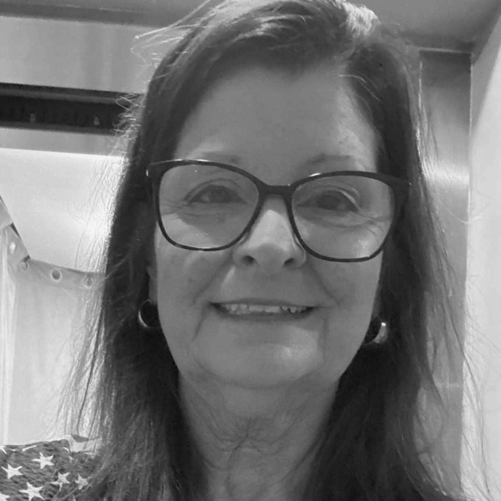 Smiling woman wearing glasses in a black-and-white selfie indoors