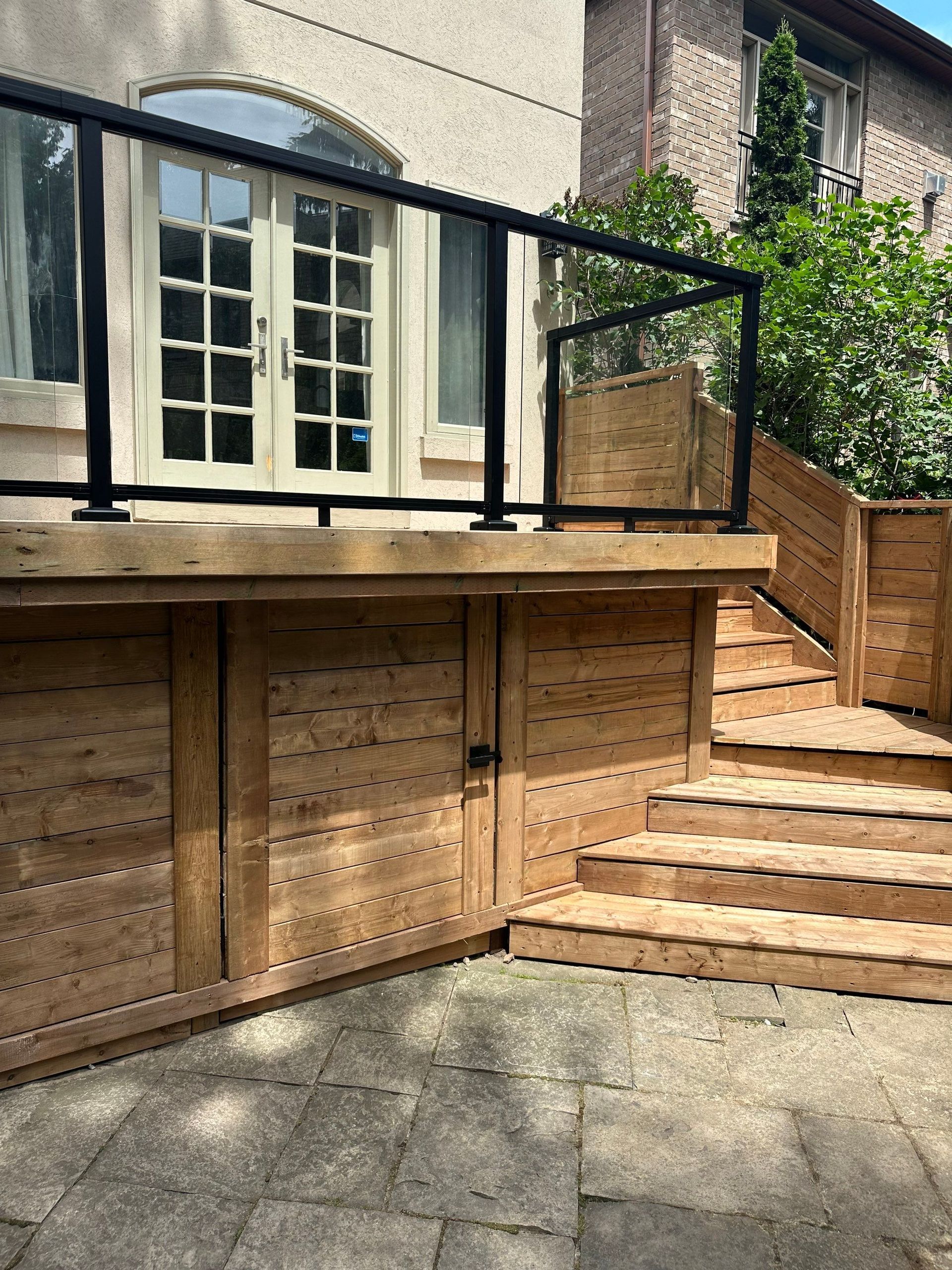 A wooden deck with stairs leading up to it and a glass railing.