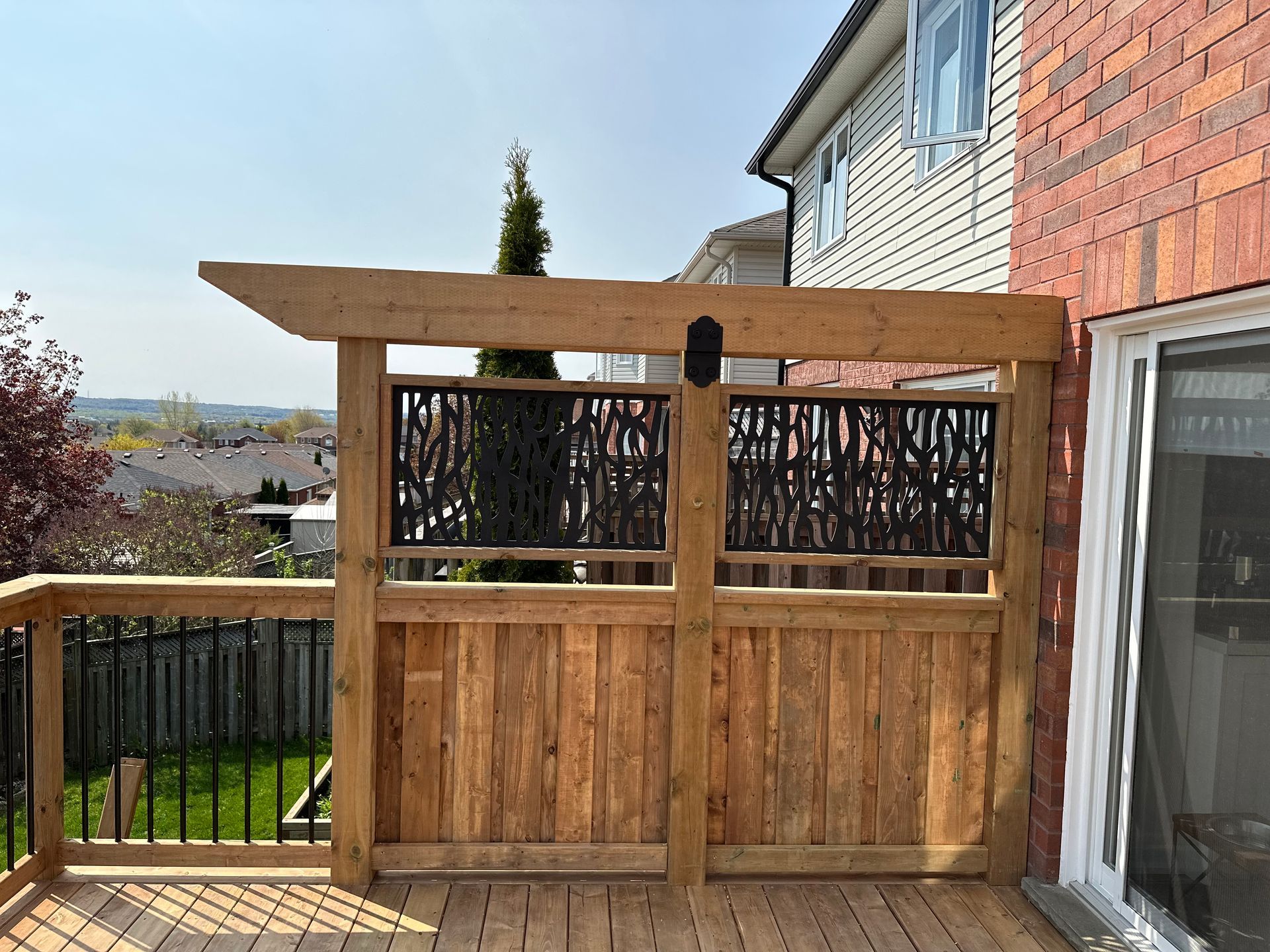 A wooden deck with a pergola and a fence in front of a brick house.