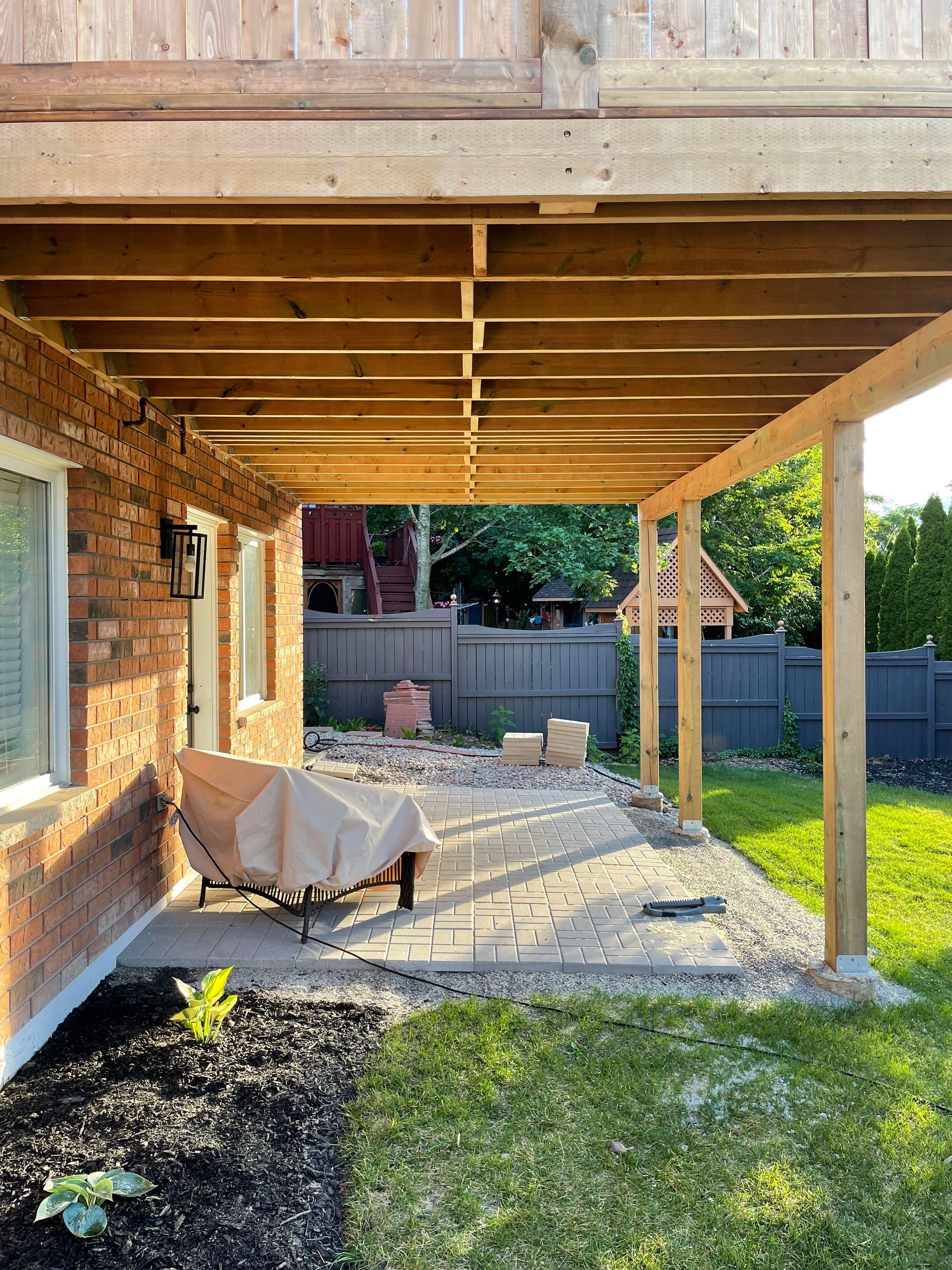 A wooden deck is being built in the backyard of a brick house.
