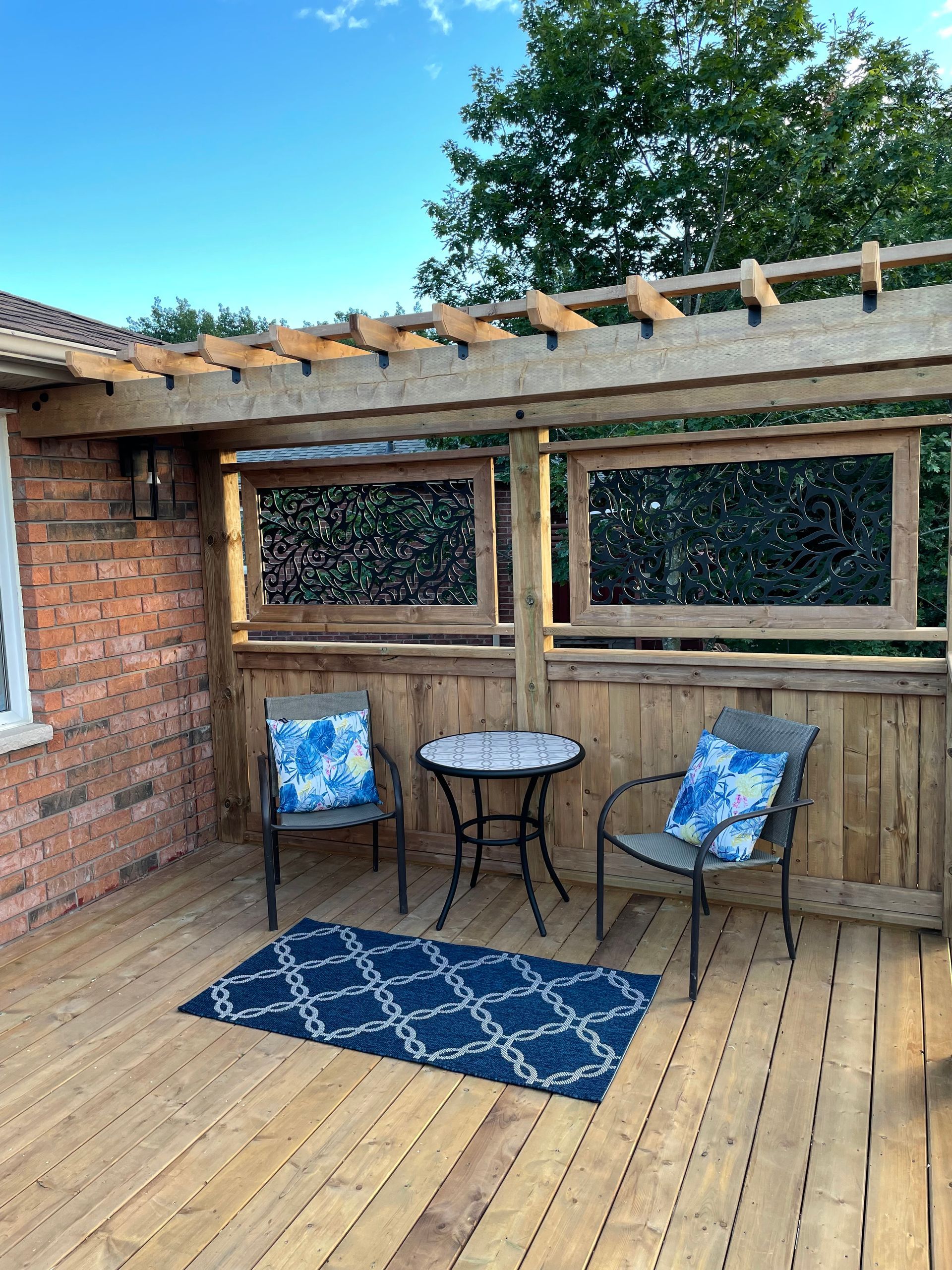 A wooden deck with two chairs and a table under a pergola.