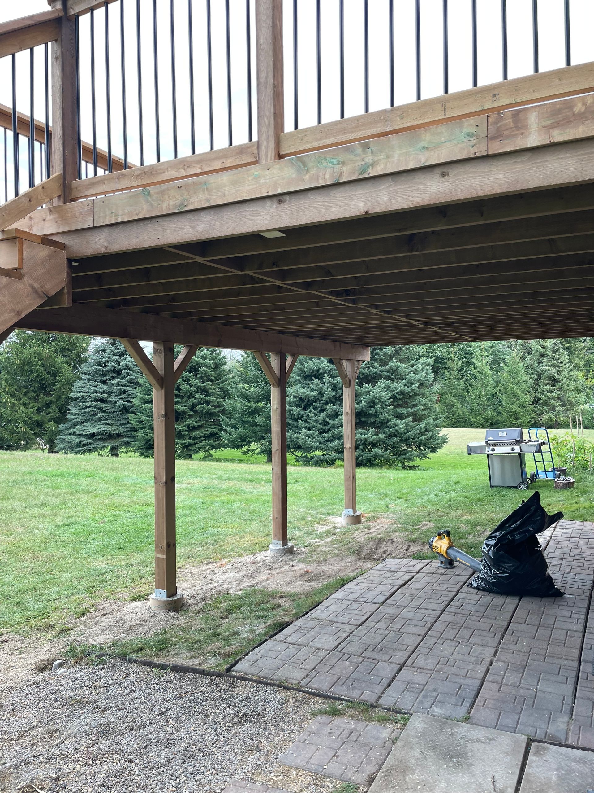 A wooden deck with a metal railing is being built in a backyard.