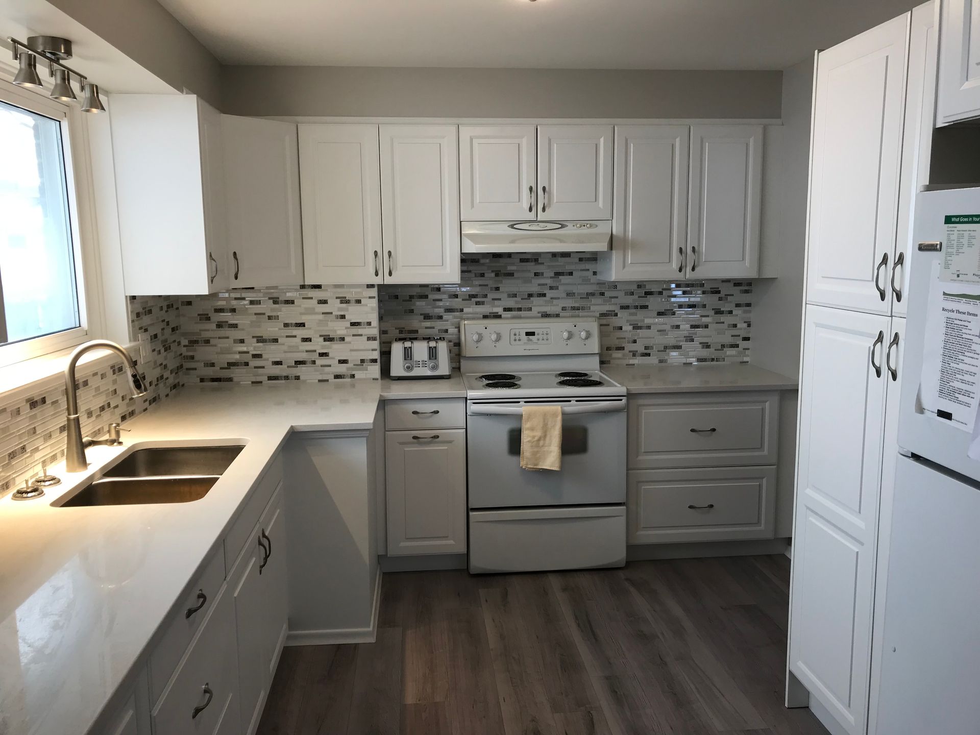 A kitchen with white cabinets a stove a sink and a refrigerator